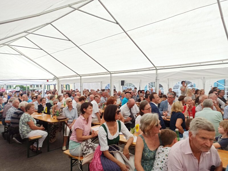 Volles Festzelt mit Gästen an langen Tischen