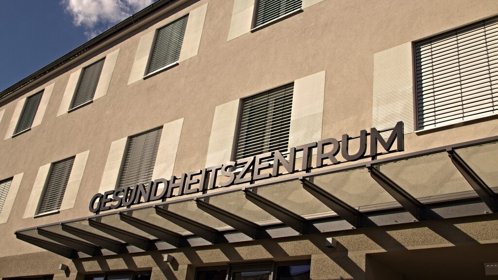 Überdachter Eingang des Gesundheitszentrums mit Schriftzug an der Fassade