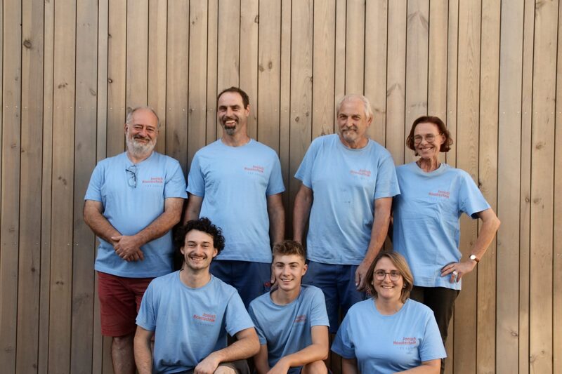 Das Team von Janisch Haustechnik in blauen Jubiläums-Shirts vor einer Holzwand
