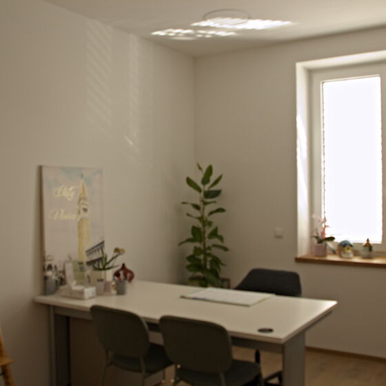 Therapie- und Ordinationsraum mit Schreibtisch, Stühlen und Fenster